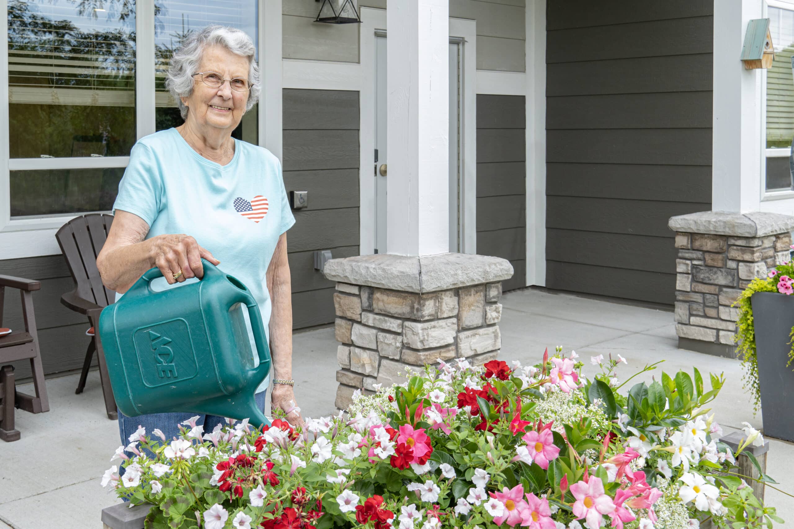 Mill-City-Senior-Living-Flower-Garden A Woman Holding A Watering Can In Front Of A Flower Bed